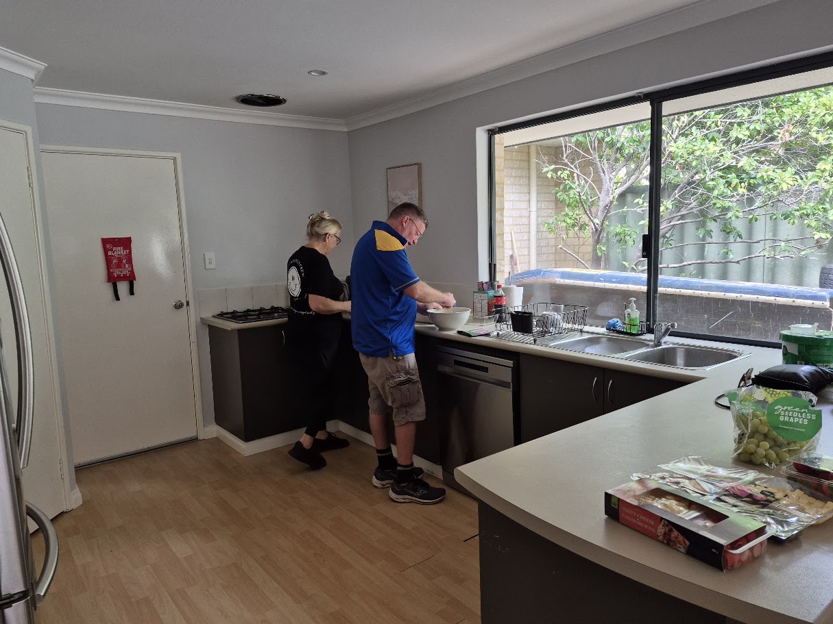 An adult participant preparing food at home with a familiar Happiness Crew member nearby.